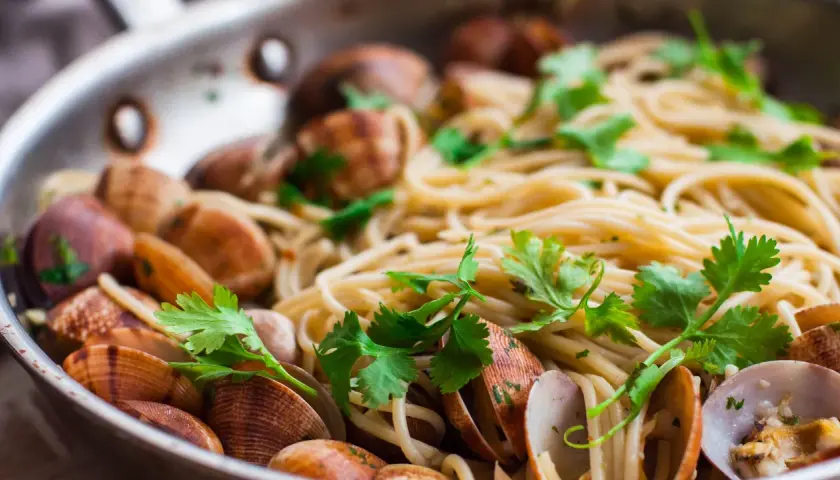 Spaghetti alle vongole surgelate, un piatto gustoso con pasta, cozze e prezzemolo fresco in una padella.