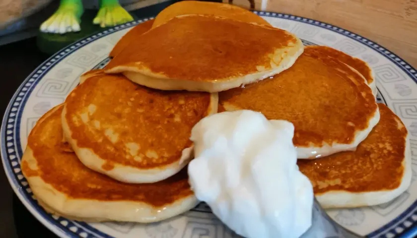 Pancake senza uova con yogurt, una pila dorata su un piatto decorato, pronta per essere gustata.