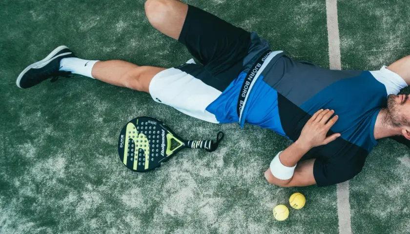 Giocatore di padel esausto, con racchetta e palline accanto. Forse ha appena eseguito un potente head smash.