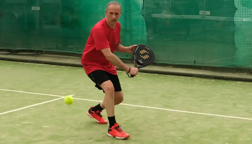 Uomo in campo da padel, pronto a colpire la palla. Un momento di gioco intenso nel padel Italia.