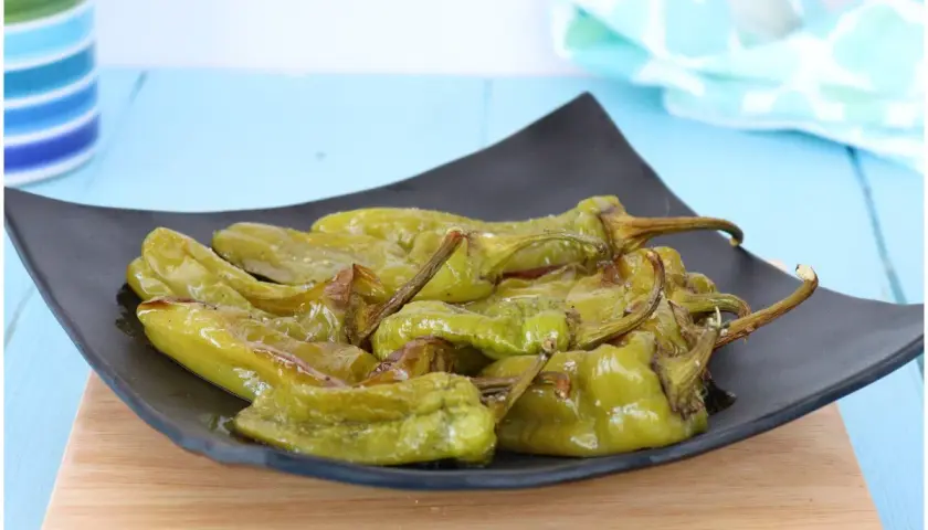 Friggitelli al forno, verdi e succosi, serviti su un piatto nero. Un contorno semplice e gustoso.