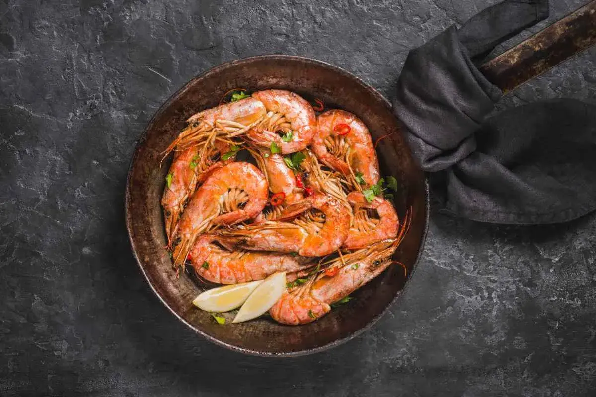 Gamberi in padella, succulenti e profumati, pronti per essere gustati con spicchi di limone fresco e un tocco di peperoncino.