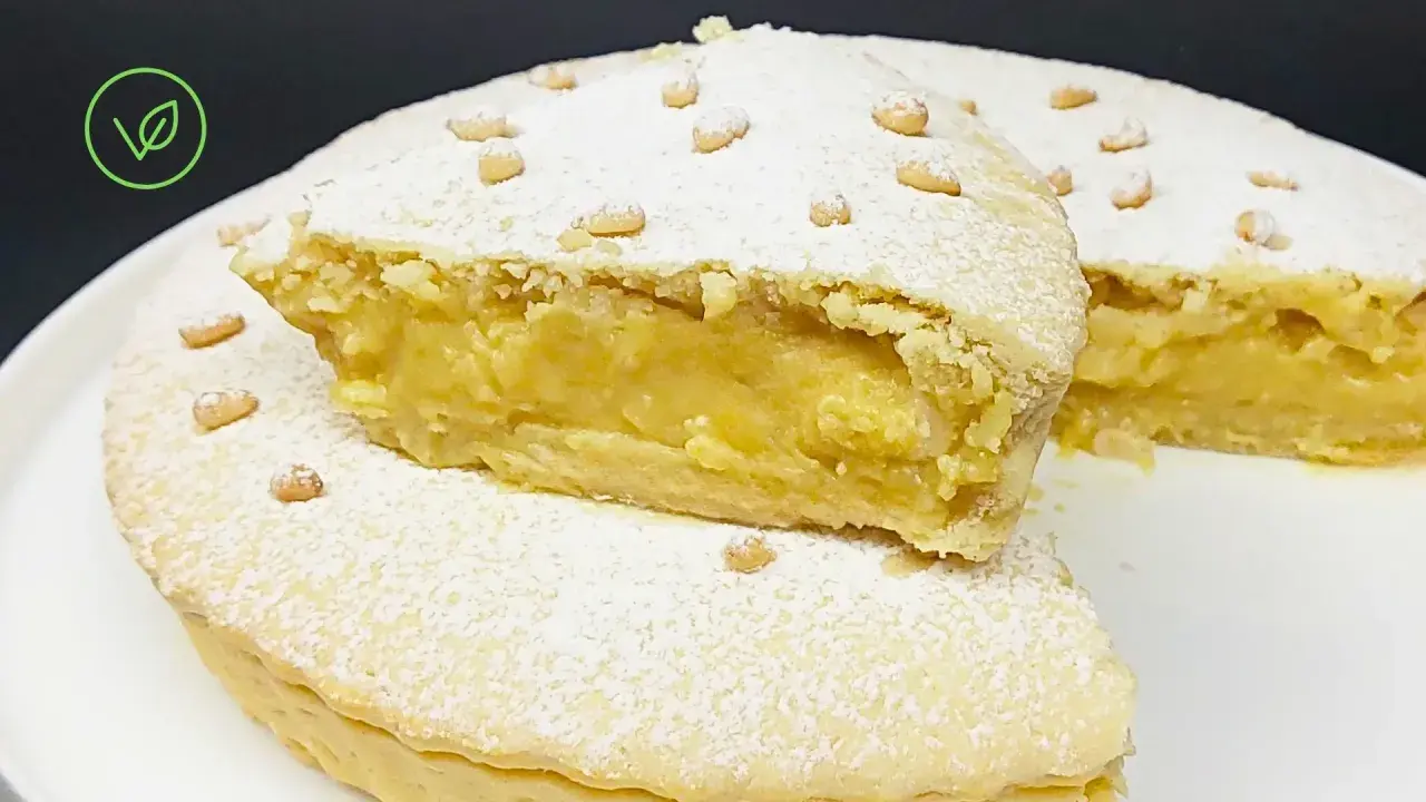 Torta vegana con crema gialla, ricoperta di zucchero a velo e pinoli. Un dolce delizioso e invitante.