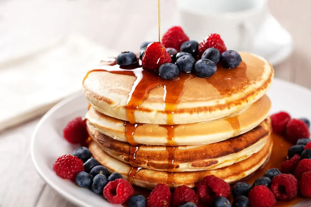 Pancakes con farina di avena, guarniti con frutti di bosco freschi e sciroppo d'acero che cola.