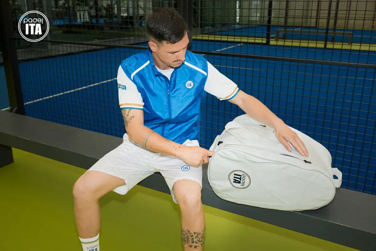 Un giocatore di padel con abbigliamento sportivo bianco e blu, pronto per giocare. Scopri come vestirsi per giocare a padel con stile e comfort.