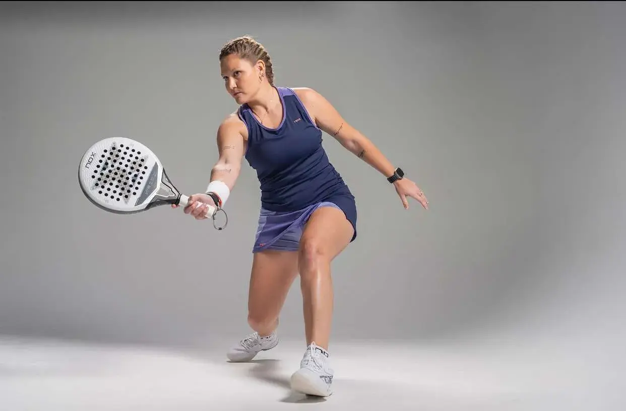 Giocatrice di padel in azione, con racchetta in mano, pronta a colpire la palla. La sua concentrazione è palpabile, un vero esempio di passione per il **padel**.