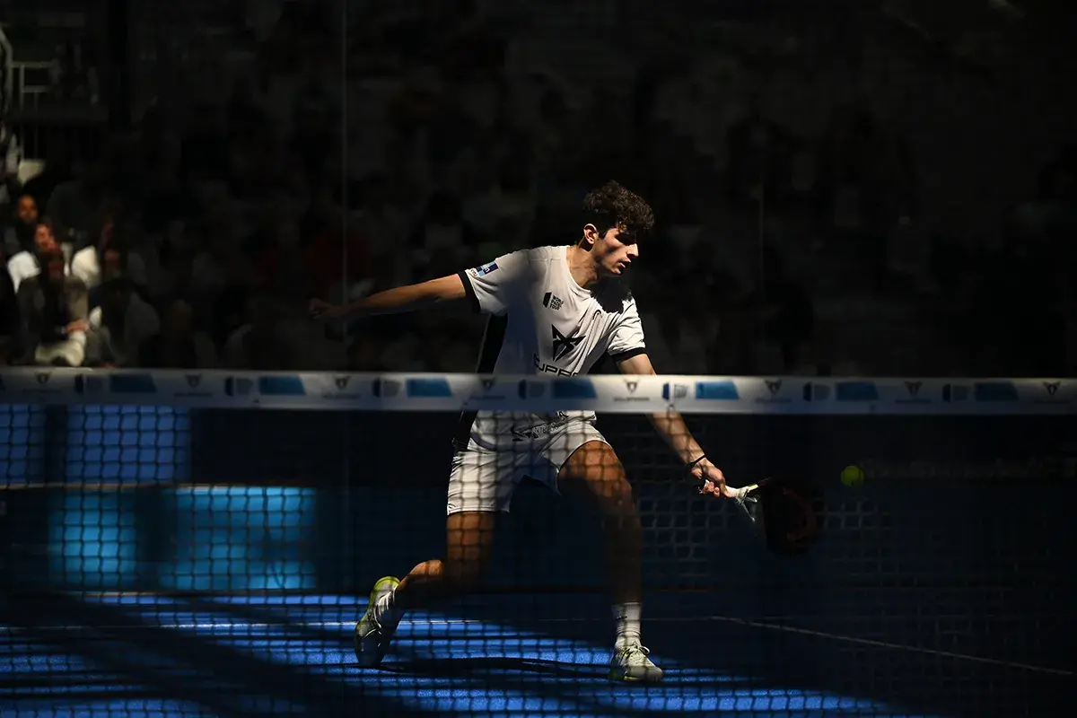 Arturo Coello in azione, colpisce la palla con la racchetta da padel, concentrato sul campo blu illuminato.