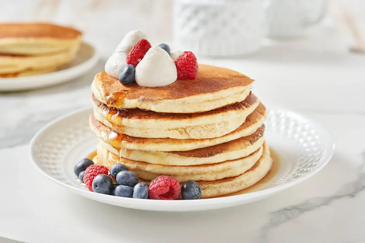 Pancakes dietetici con panna montata, mirtilli e lamponi, inzuppati nello sciroppo d'acero.