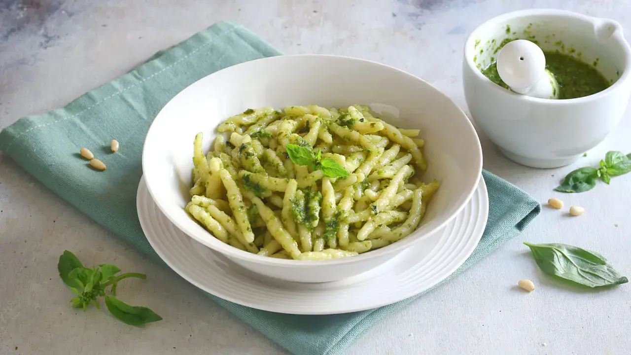 Un piatto di pasta al pesto fresco, con basilico e pinoli sparsi, pronto per essere gustato.