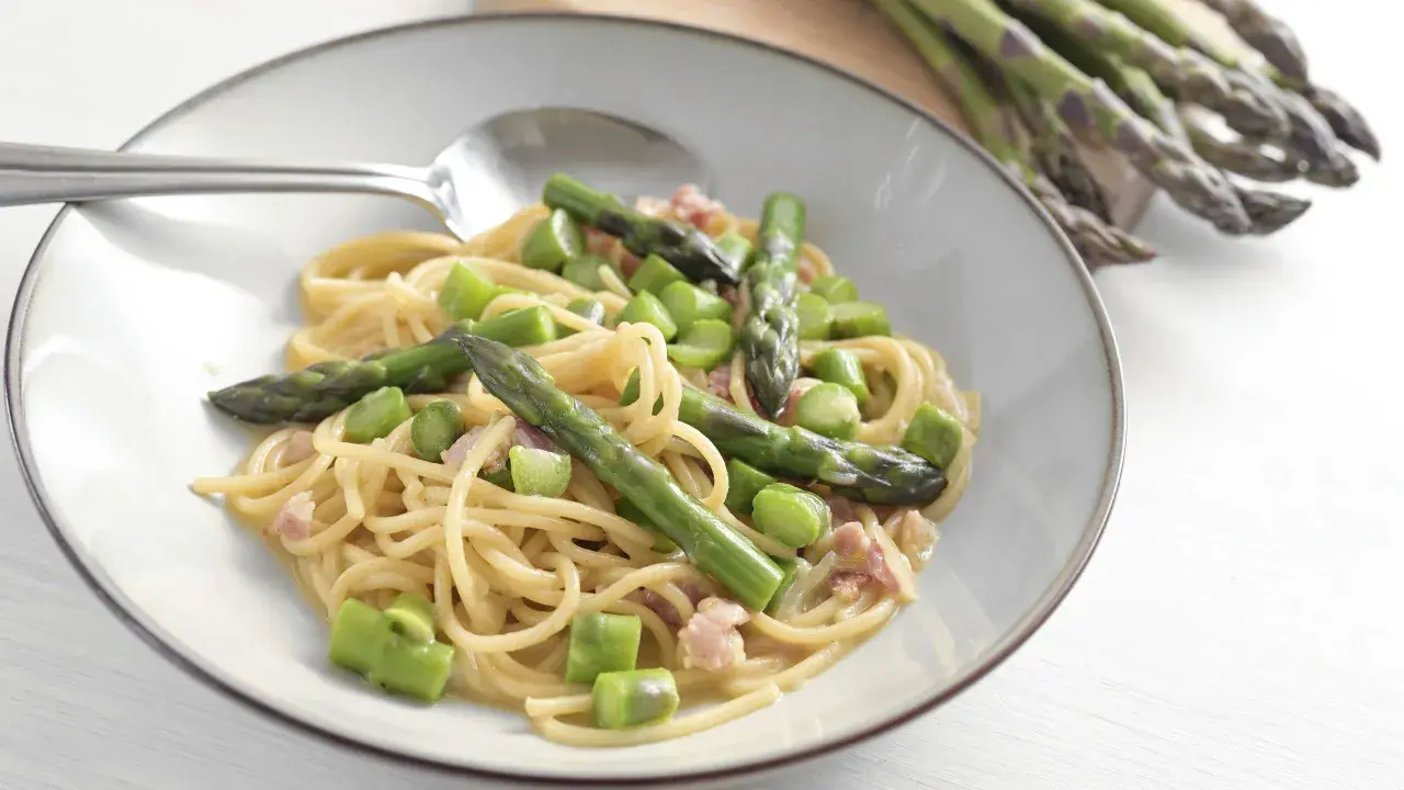 Un piatto di spaghetti con asparagi freschi e cubetti di speck croccante, condito con una cremosa salsa.
