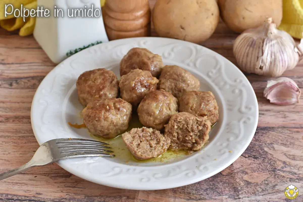 Polpette in umido succulente su un piatto bianco, con patate e aglio sullo sfondo. Una forchetta è pronta per gustarle.