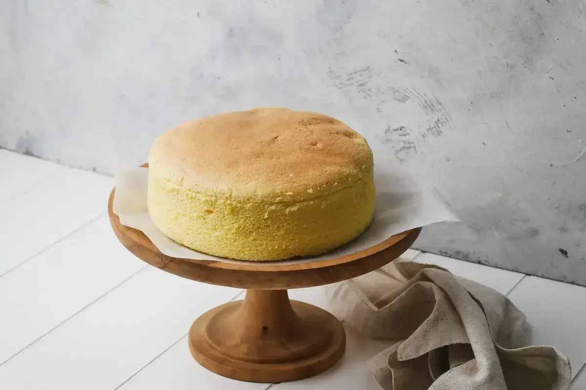 Una soffice torta con albumi, dorata e leggera, su un alzata di legno. Perfetta per una colazione o merenda.