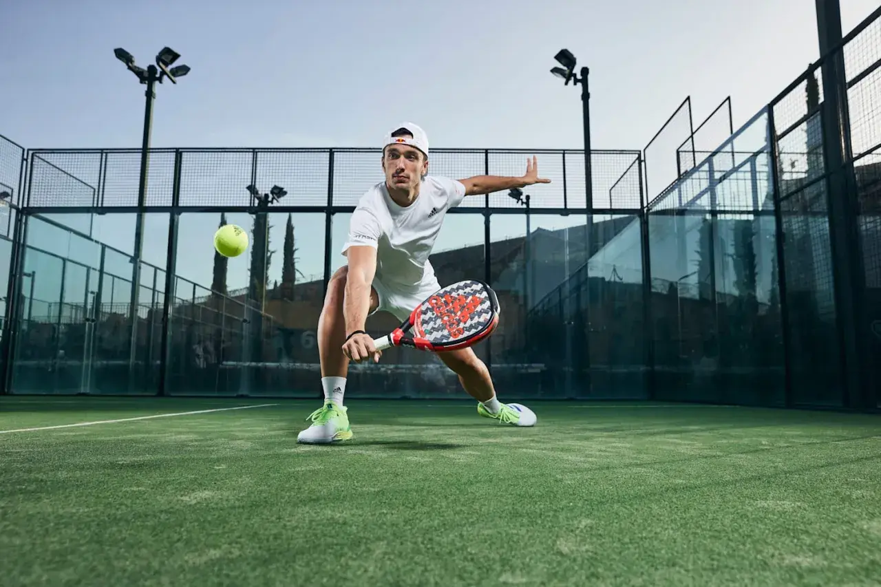 Ale Galán in azione, con le sue scarpe da padel che spiccano sul campo verde. Colpisce la palla con determinazione.