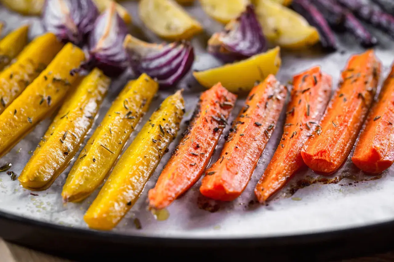 Carote gialle e arancioni, cipolle rosse e patate dorate, condite con erbe aromatiche, pronte per essere gustate come deliziose verdure miste al forno.