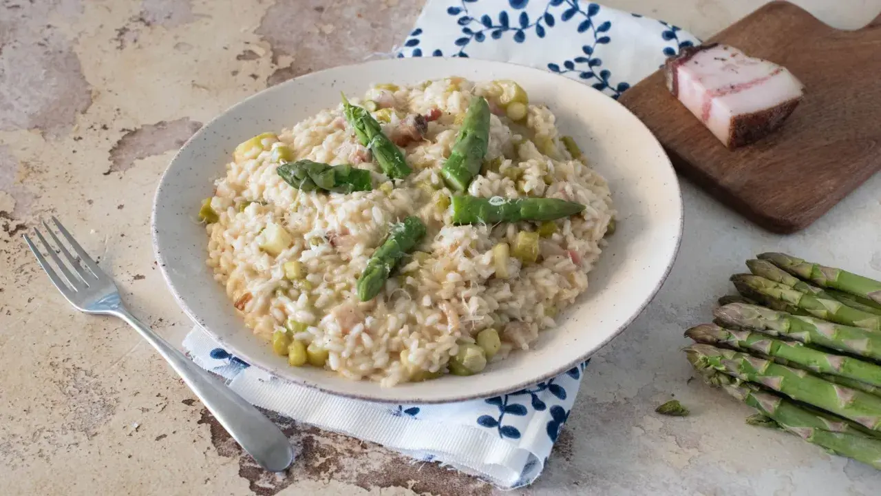 Un cremoso risotto con asparagi e pancetta, guarnito con punte di asparagi freschi e una spolverata di parmigiano.