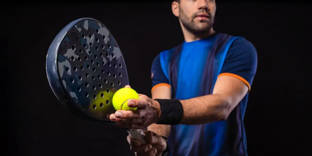 Giocatore di padel con racchetta e pallina, pronto a migliorare il suo gioco.