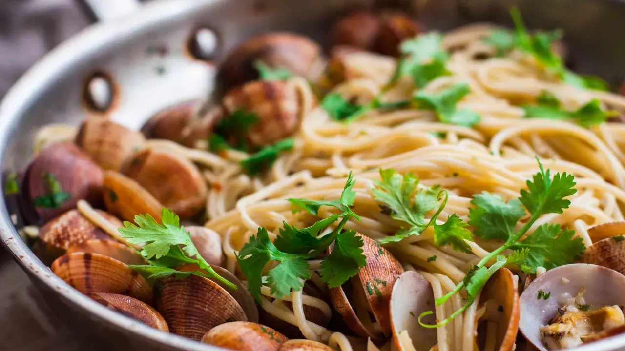 Spaghetti alle vongole surgelate, un piatto gustoso con pasta, cozze e prezzemolo fresco in una padella.