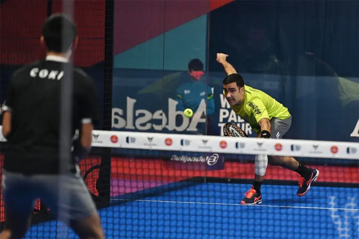 Giocatore di padel in maglia verde colpisce la palla, con un avversario di spalle. Il **chiquita significato** in questo sport è un colpo basso e angolato.