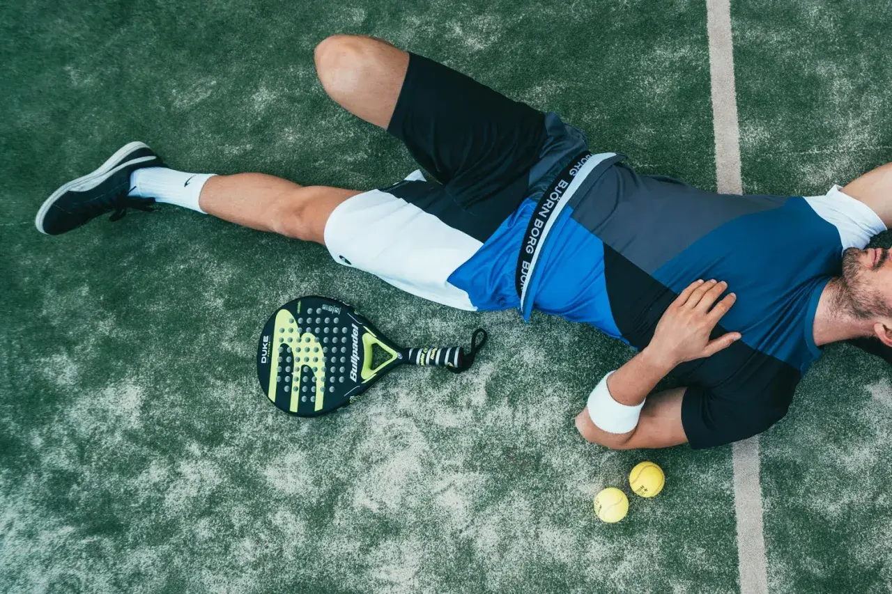 Giocatore di padel esausto, con racchetta e palline accanto. Forse ha appena eseguito un potente head smash.