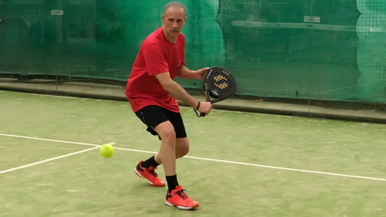 Uomo in campo da padel, pronto a colpire la palla. Un momento di gioco intenso nel padel Italia.