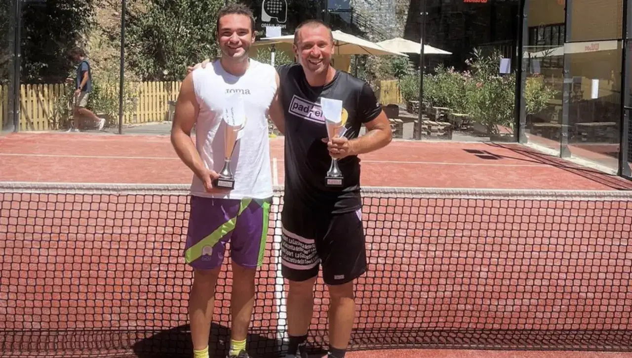Vincitori di un torneo di padel a Cassano, sorridono con i loro trofei su un campo da padel.
