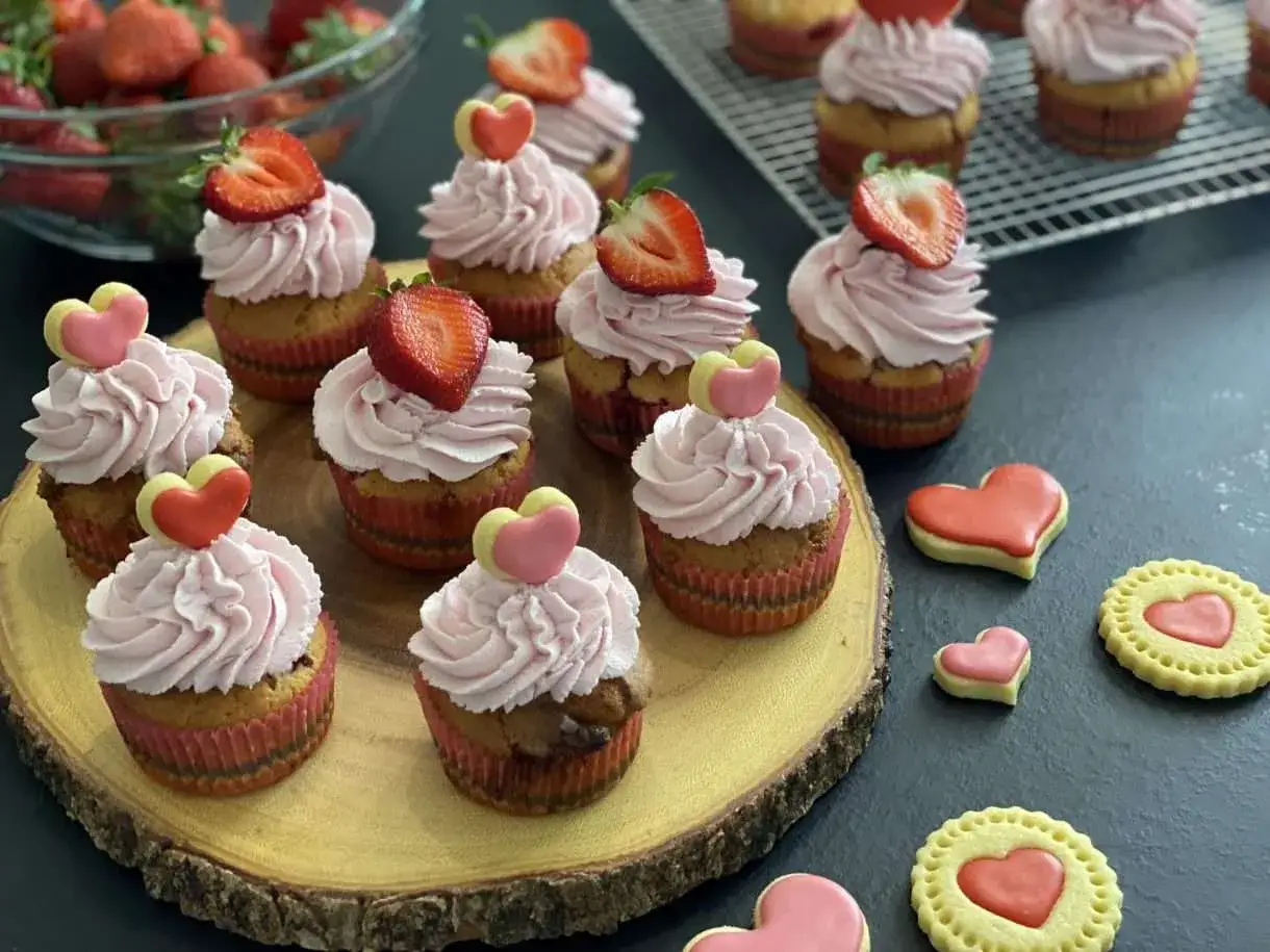 Deliziosi muffin alle fragole con glassa rosa e decorazioni a cuore, pronti per San Valentino.