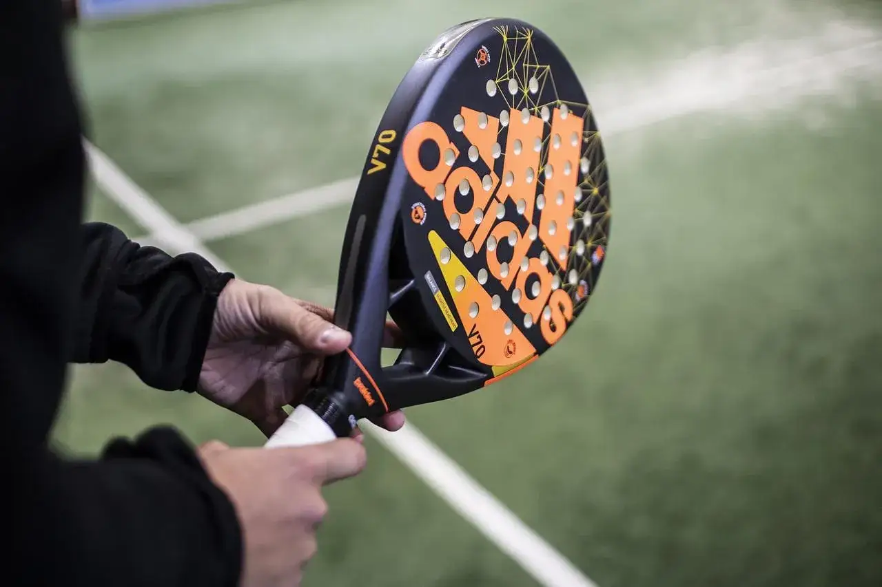 Mani che impugnano una racchetta da padel Adidas V70. Si nota la differenza tra il grip originale e un overgrip bianco aggiunto per migliorare la presa.