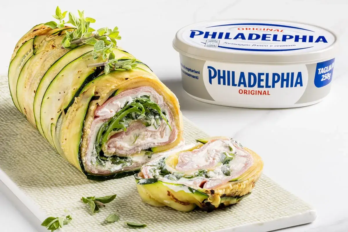 Rotolo di zucchine ripieno di prosciutto, formaggio Philadelphia e rucola, guarnito con erbe aromatiche.