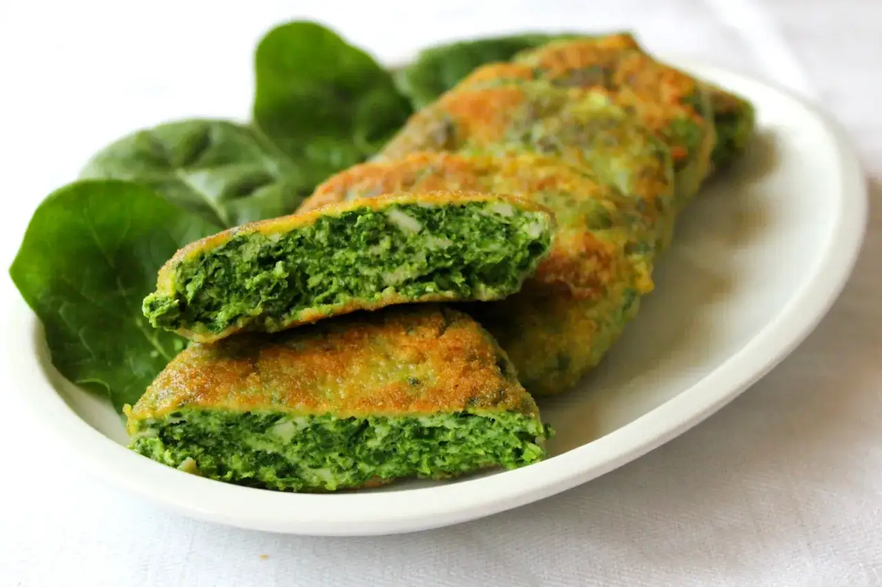 Deliziose spinacine fatte in casa, dorate e croccanti fuori, morbide e verdi dentro, servite su un piatto bianco con foglie di spinaci freschi.