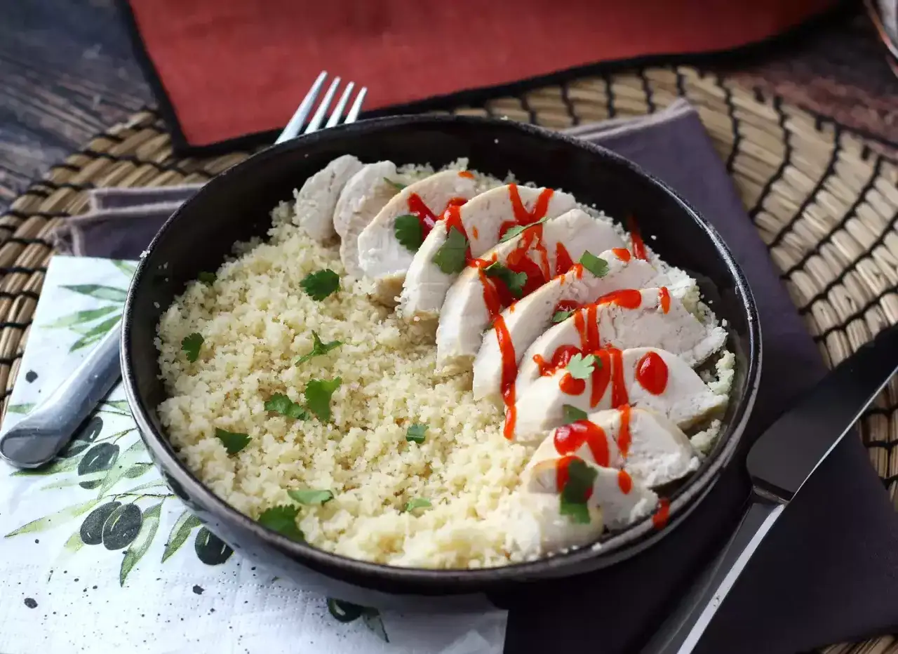 Pollo in padella a fette, servito su couscous e guarnito con salsa piccante e coriandolo. Un piatto gustoso e colorato.