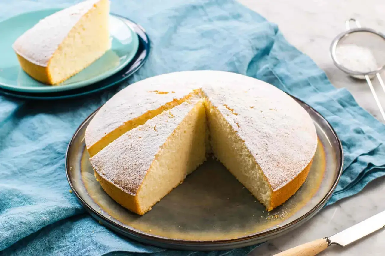 Torta soffice con albumi, spolverata di zucchero a velo, su un piatto con una fetta tagliata.