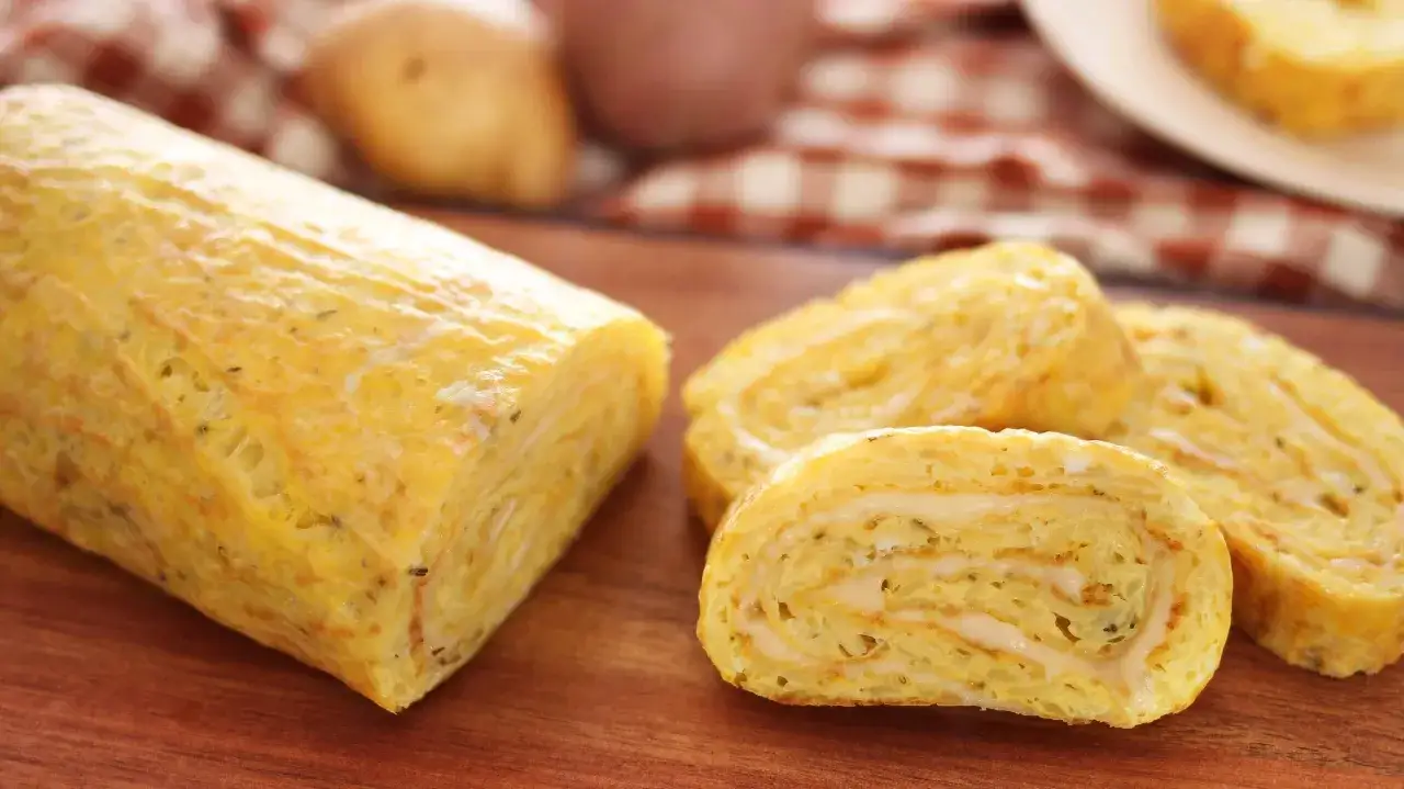 Un rotolo dorato di polpettone di patate, tagliato a fette, rivela un ripieno cremoso.
