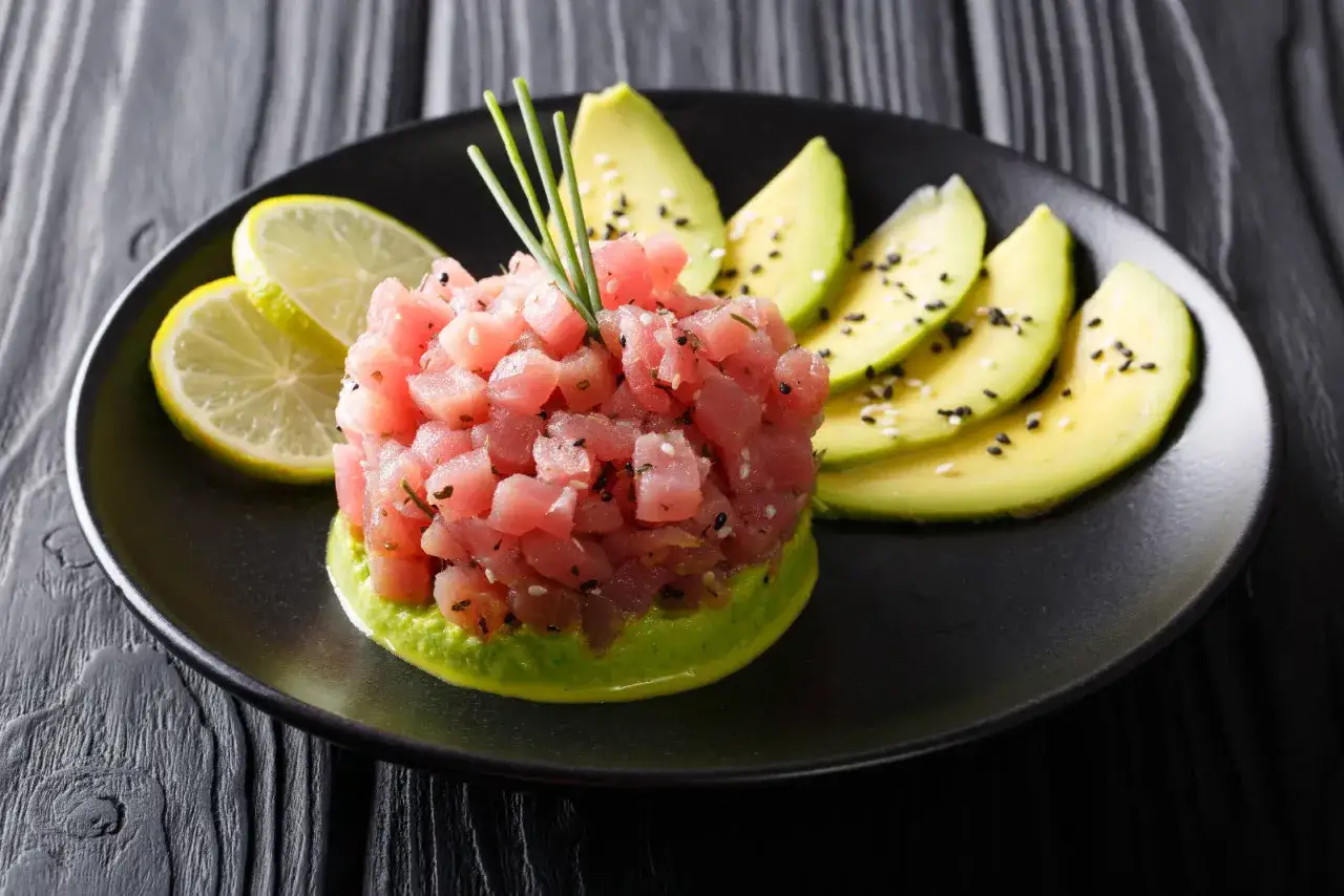 Tartare di tonno fresca e colorata, servita su un letto di avocado cremoso, con spicchi di lime e semi di sesamo.