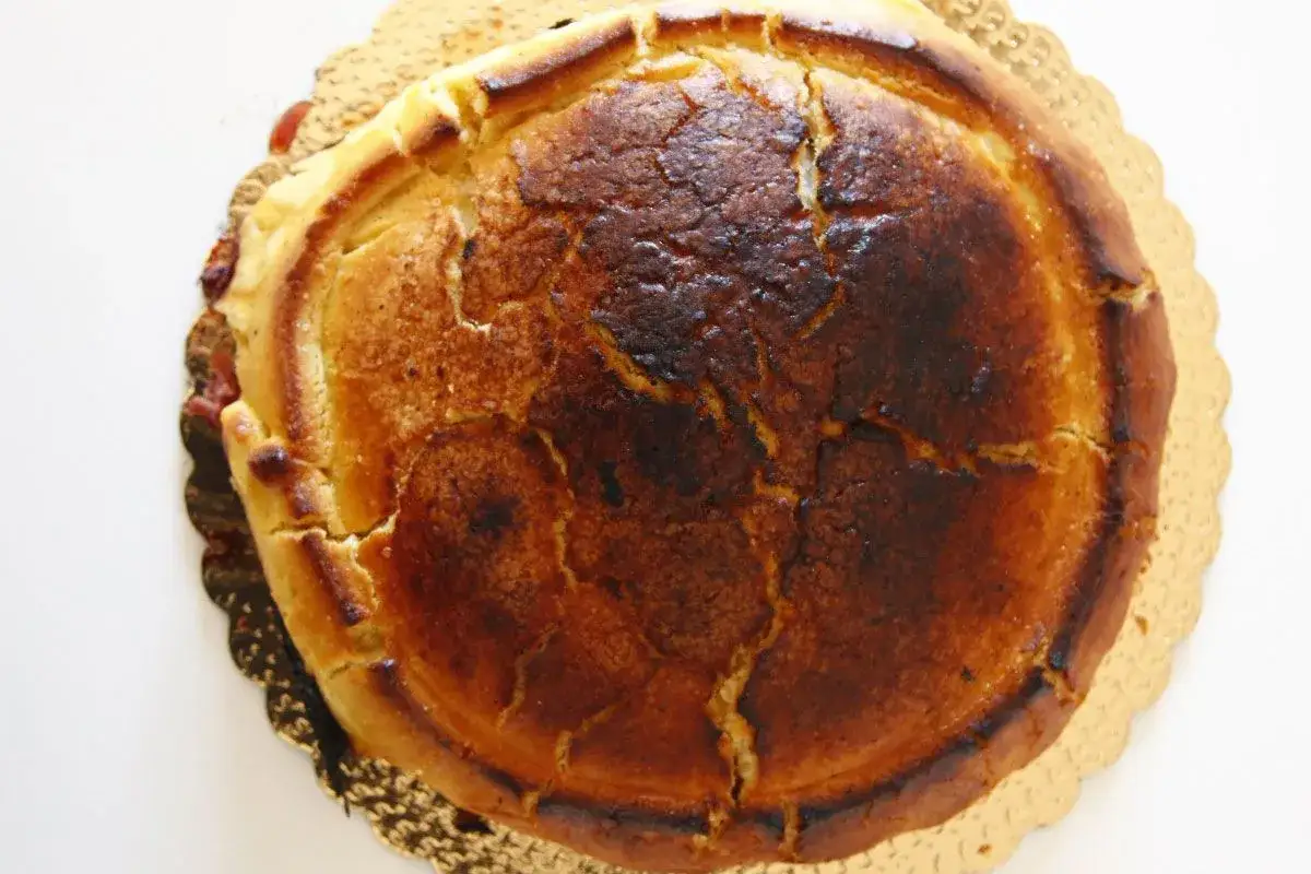 Crostata ricotta e visciole dorata, con la crosta leggermente bruciacchiata e crepe che rivelano il ripieno dolce.