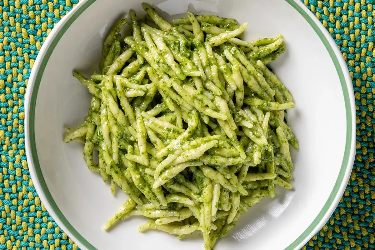 Un piatto di trofie al pesto, con la pasta fresca avvolta in un sugo verde brillante, pronta per essere gustata.
