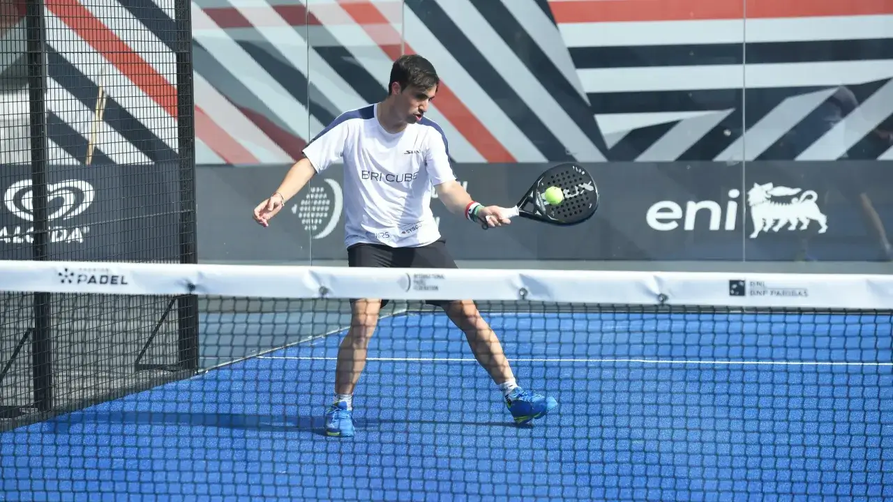 Giocatore di padel in azione, colpisce la palla con la racchetta. La sua concentrazione è palpabile mentre si prepara per il prossimo punto.