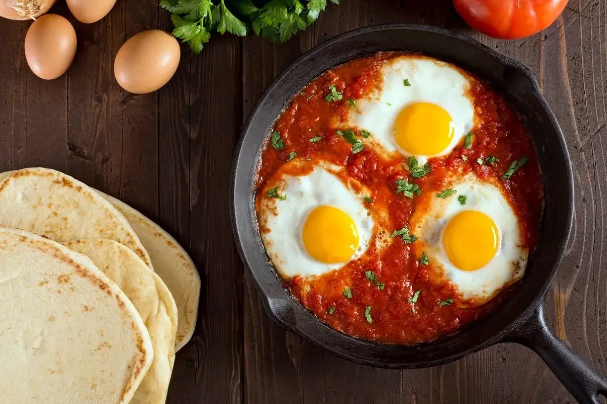 Uova in purgatorio in padella, con pomodoro e prezzemolo, accompagnate da pane arabo.