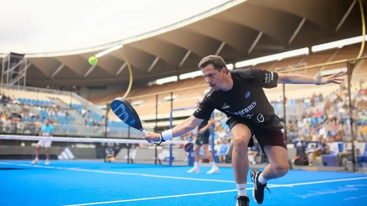 Paquito Navarro in azione, colpisce la palla con la racchetta da padel su un campo blu, con il pubblico sugli spalti.