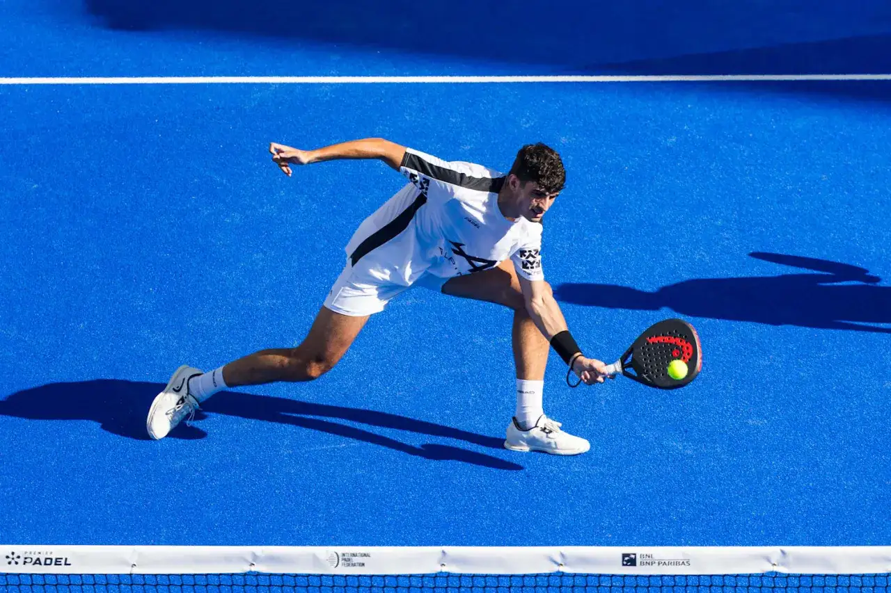 Giocatore di padel in azione, colpisce la palla con la racchetta. Un perfetto servizio padel sotto il sole.