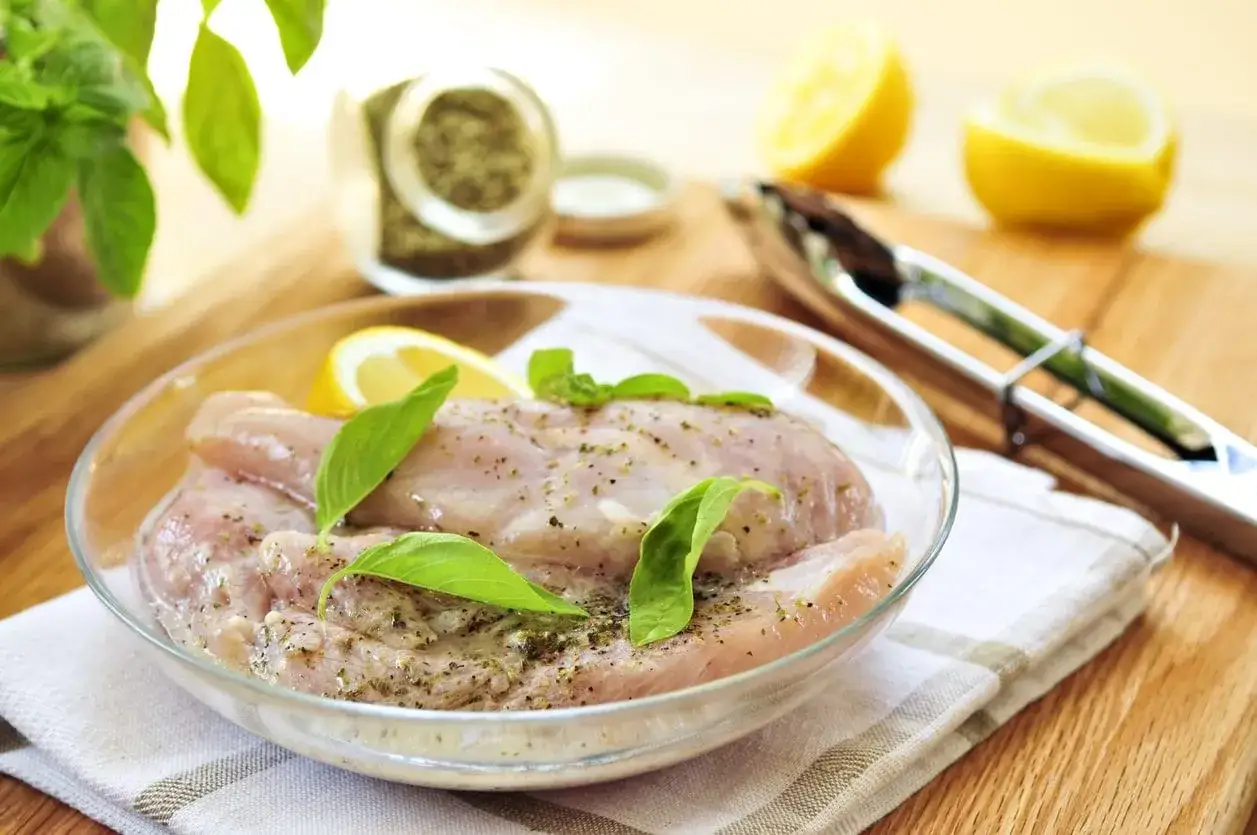 Petto di pollo pronto per la marinatura, con limone e basilico fresco. Ingredienti per un sapore delizioso.
