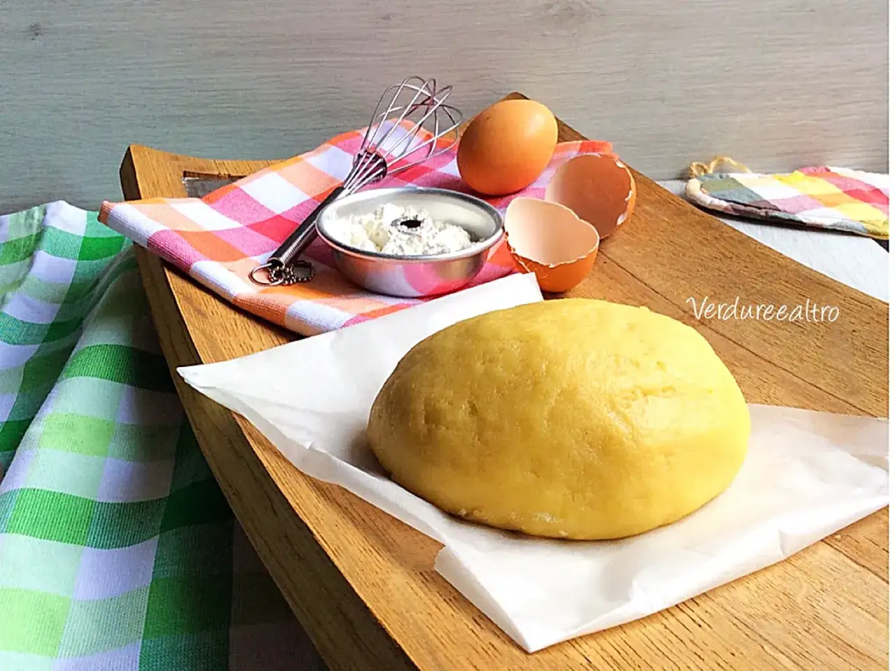 Impasto giallo per pasta frolla con olio, uova e frusta su tagliere di legno.