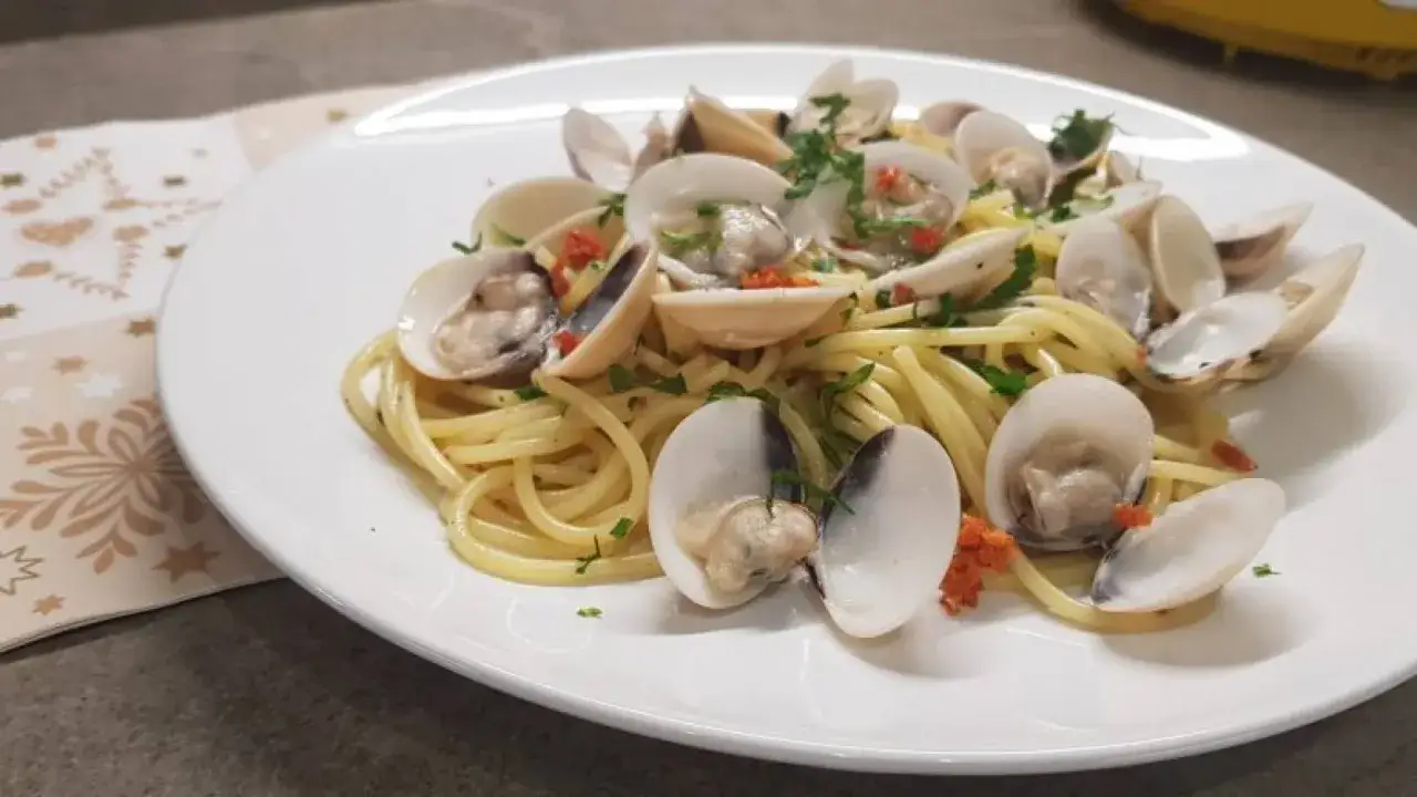 Spaghetti alle vongole surgelate, un classico piatto di mare, servito su un piatto bianco con prezzemolo tritato e peperoncino.