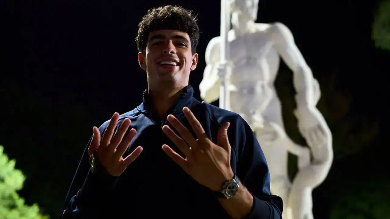 Giovane campione di padel sorride con le mani aperte, con una statua classica sullo sfondo.