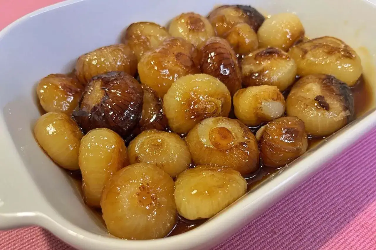 Cipolline caramellate in agrodolce, dorate e lucide, servite in una ciotola bianca su un tovagliolo rosa.