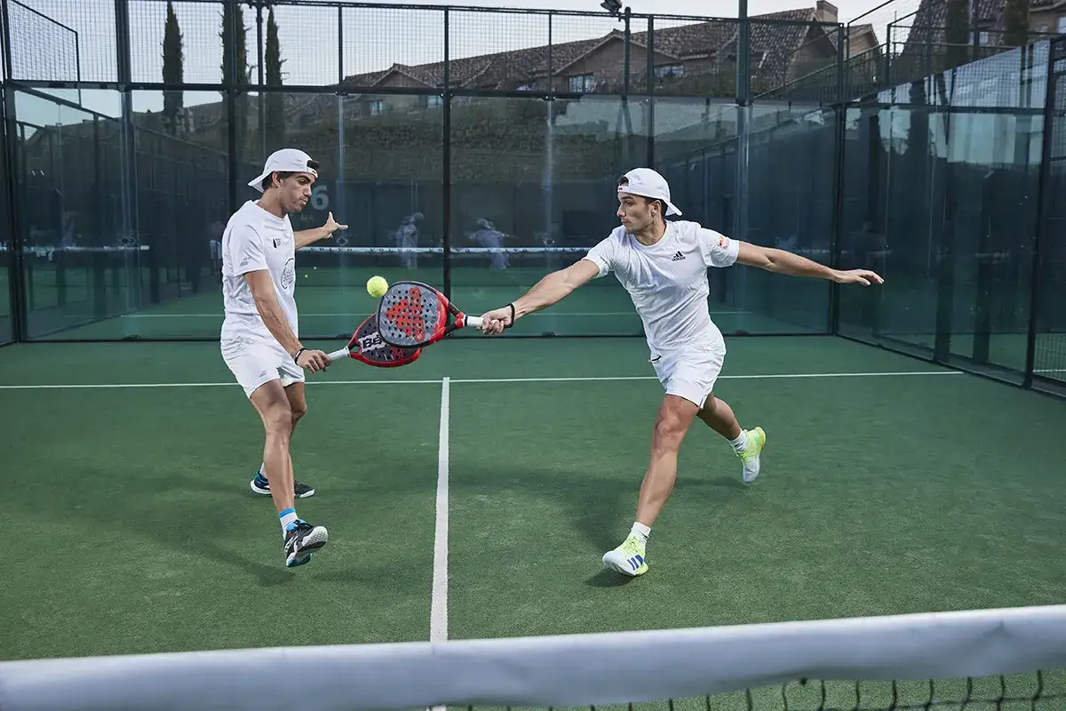 Due giovani giocatori di padel, in tenuta bianca, si sfidano in un'intensa partita. Le nuove coppie padel mostrano agilità e tecnica.