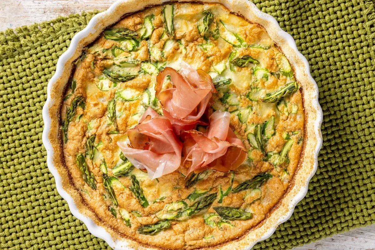 Frittata di asparagi al forno, dorata e invitante, guarnita con fette di prosciutto crudo.