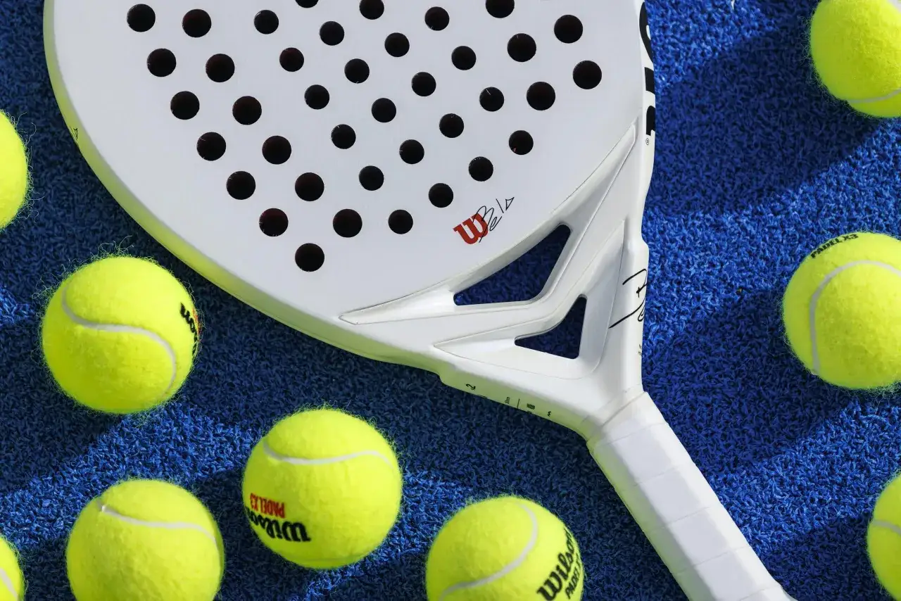 Racchetta da padel bianca Wilson con palline gialle su campo blu. Pronto per una partita di padel x3!