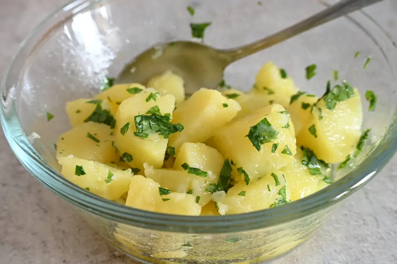 Patate prezzemolate in una ciotola di vetro, condite con erbe fresche e un cucchiaio.