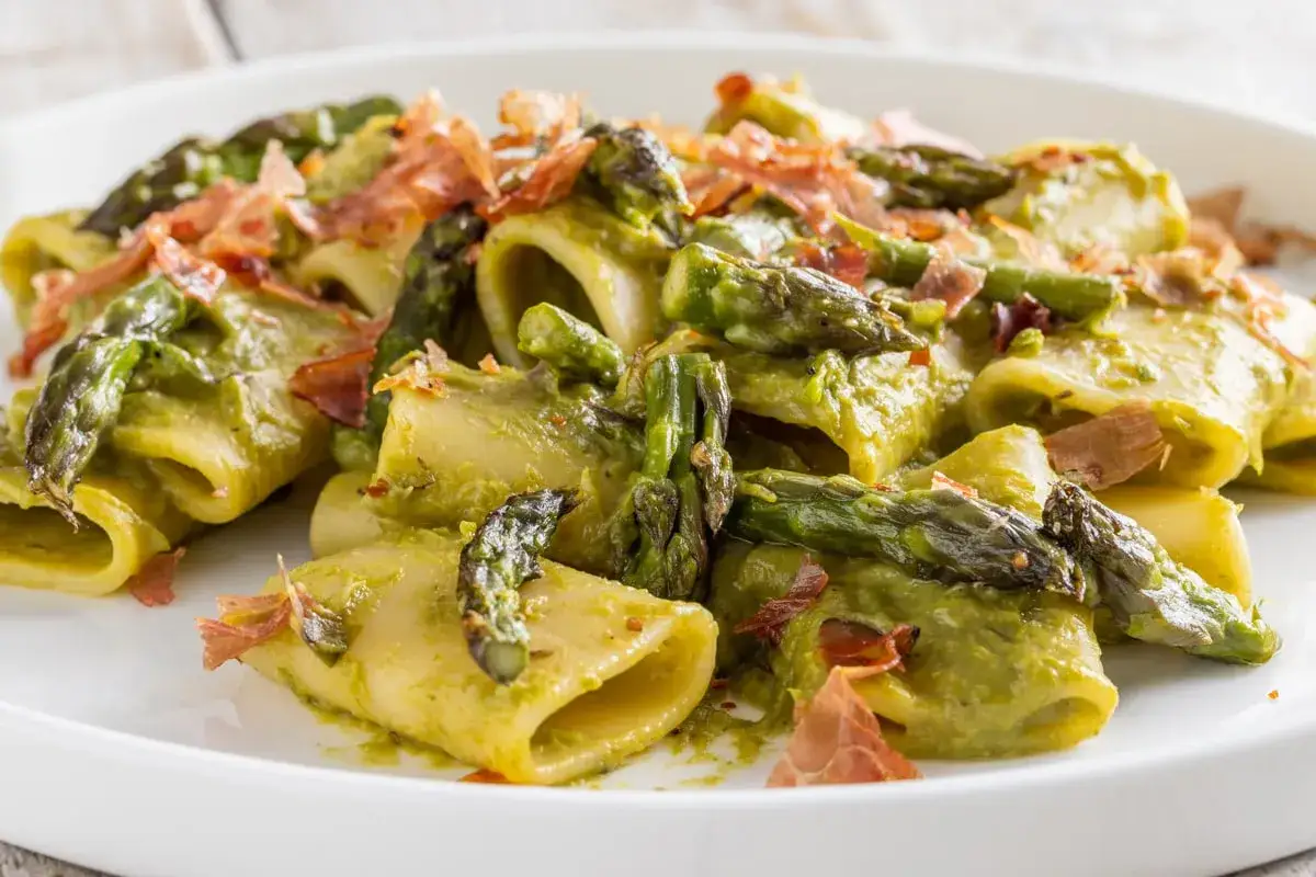 Paccheri conditi con crema di asparagi, punte di asparagi croccanti e scaglie di speck. Un piatto primaverile che profuma di buono.