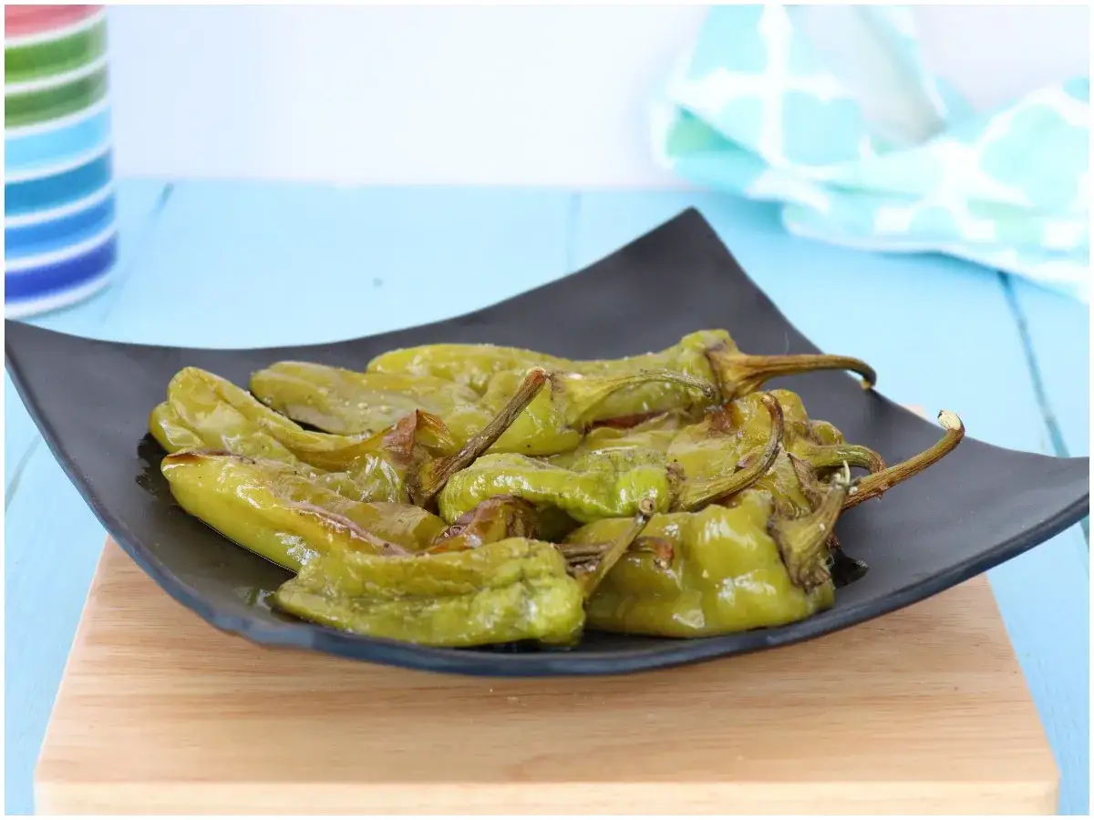 Friggitelli al forno, verdi e lucidi, serviti su un piatto nero.